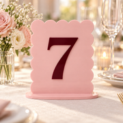 Blush pink and burgundy scalloped table number 7 in a floral wedding table setting