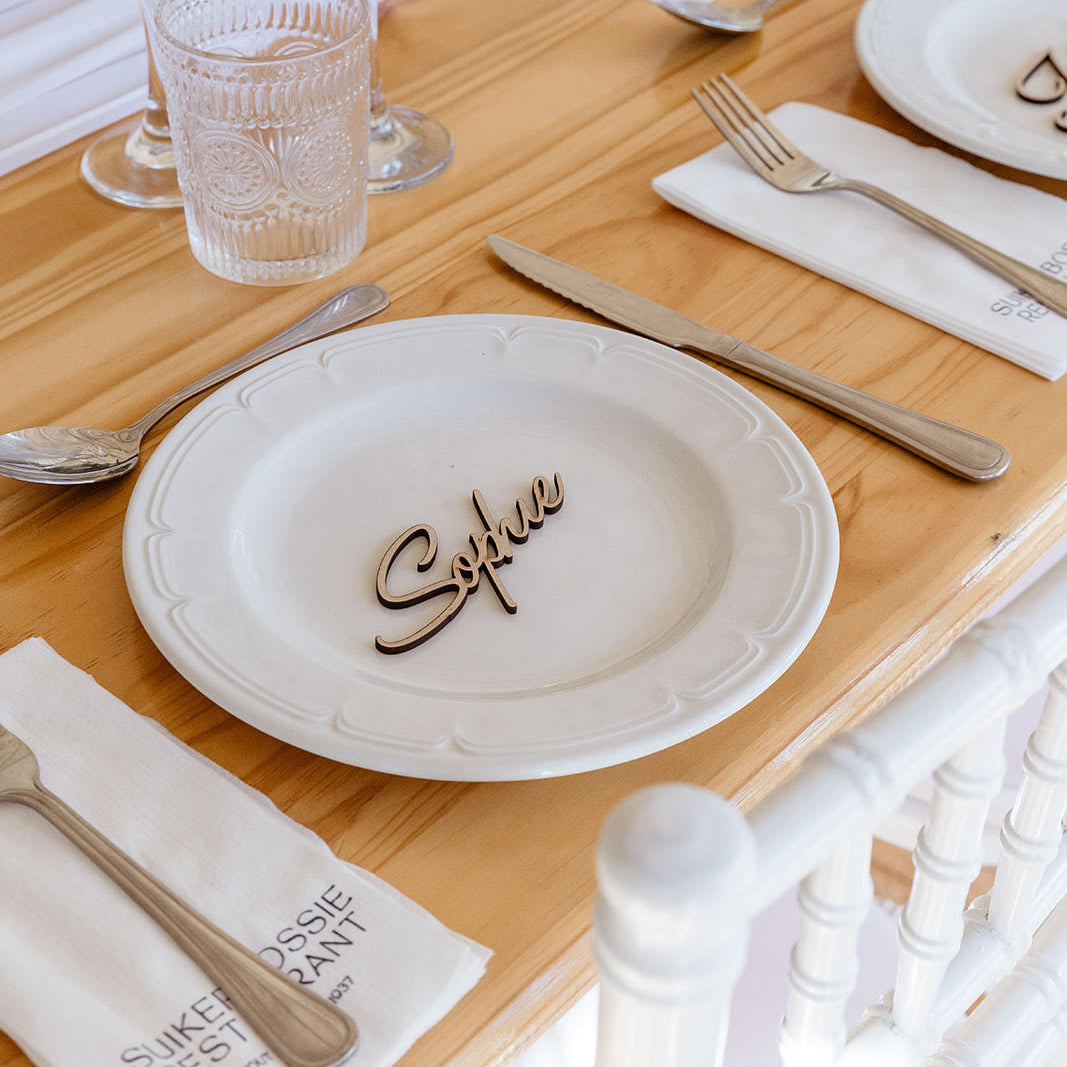 Table setting with a plate labeled 'Sophie' on a wooden table.